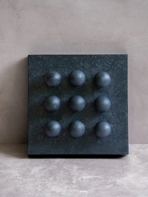 Carbon by Paola del Valle — a dark charcoal marbled square panel set with a three-by-three grid of nine deep grey-blue orbs.