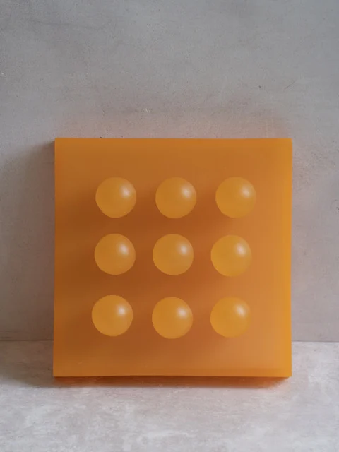 Citrus by Paola del Valle — a translucent amber-orange resin square panel set with a three-by-three grid of nine soft orange orbs.