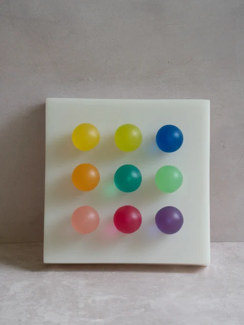 Rainbow by Paola del Valle — a milky translucent square panel set with a three-by-three grid of nine glowing orbs, each a different colour from yellow and blue to coral and violet.